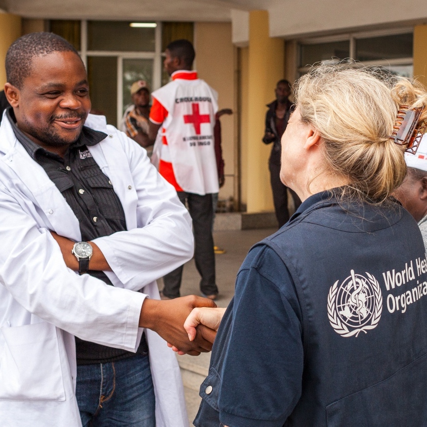 A WHO agent greets a doctor with a handshake.